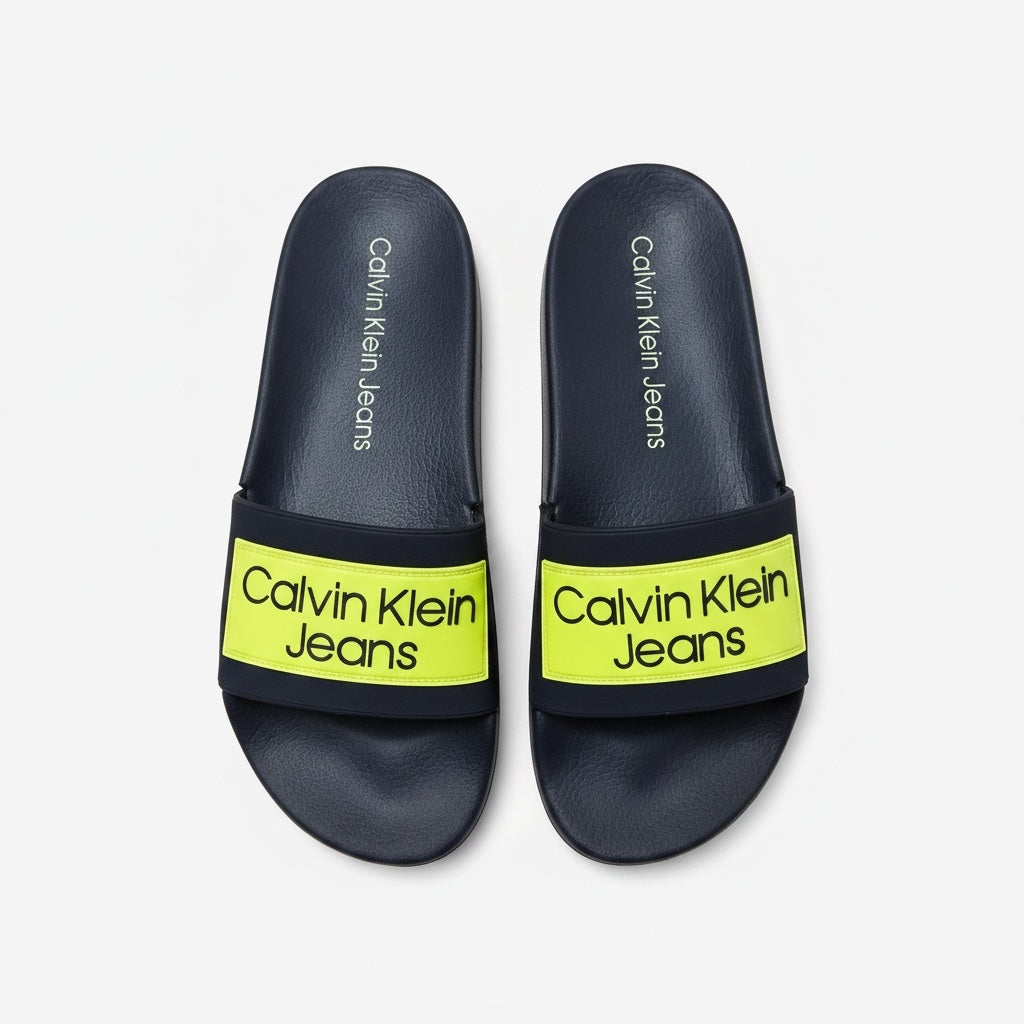 picknpack Calvin Klein Jeans navy blue pool slides with a vibrant neon yellow strap and bold logo branding.