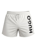 picknpack white HUGO swim shorts with a bold black vertical logo on the leg, elastic waistband, and drawstring.